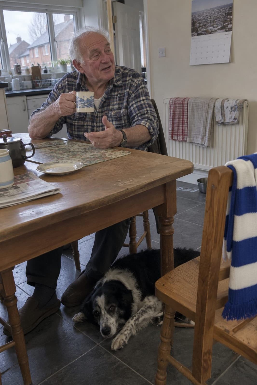 Graham at his kitchen table with a mug of tea, his dog under the table